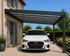 Carport aluminium adossé gris anthracite avec toiture transparente, installé contre une maison pour abriter une voiture