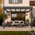 Pergola aluminium adossée gris anthracite installée sur une terrasse avec salon de jardin devant une maison